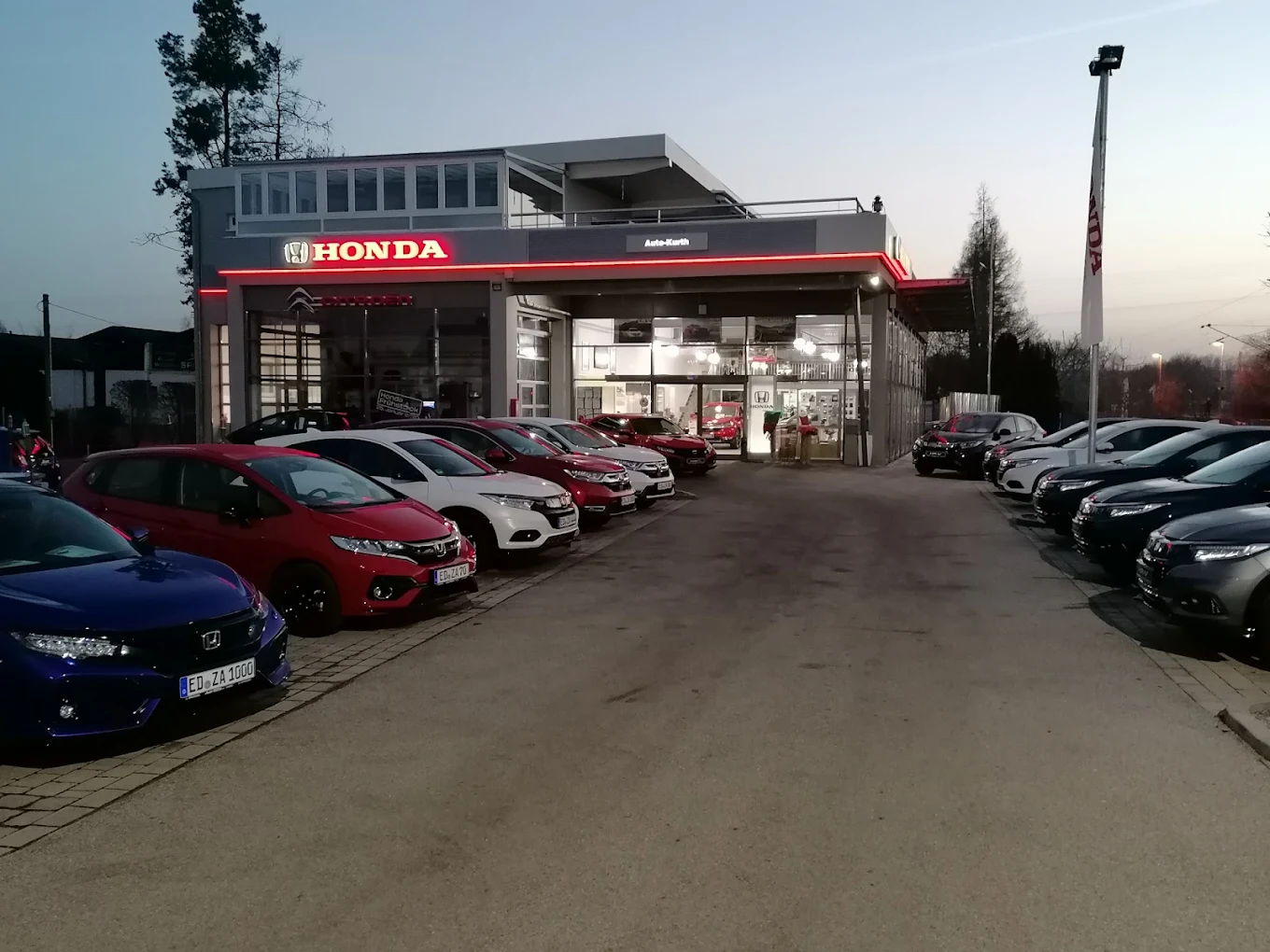Das Autohaus Auto-Kurth in Erding in der Abenddämmerung mit beleuchtetem Honda-Schriftzug und Fahrzeugen auf dem Hof